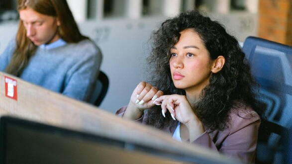 Junge Frau sitzt konzentriert an ihrem Arbeitsplatz im Büro und wirkt nachdenklich – Symbolbild dafür, Anzeichen von Gewalt oder Konflikten am Arbeitsplatz frühzeitig zu erkennen.