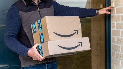 Ein Paketbote klingelt mit mehreren Amazon-Paketen an einer Haustür.