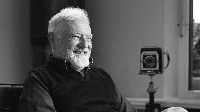 Das Bild zeigt ein Portr&auml;tfoto des Fotografen Christian Stuppner. Er lacht offen und entspannt einen Gespr&auml;chspartner an. Im Hintergrund sieht man ein altes Kameramodell.