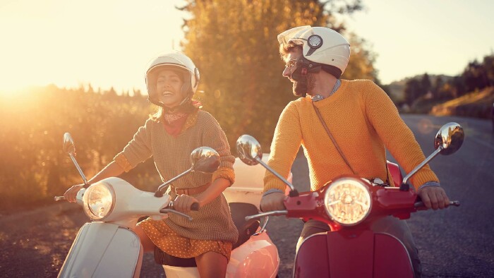 Sorglos durch Bella Italia – aber nur mit dem nötigen Know-how. Wer 2025 mit Roller, Auto oder Rad unterwegs ist, sollte die neuen Verkehrsregeln kennen. © lucky business, AdobeStock Junges Paar auf Motorrollern bei Sonnenuntergang – Italienurlaub 2025 mit neuen Verkehrsregeln für Roller, Auto und Fahrrad