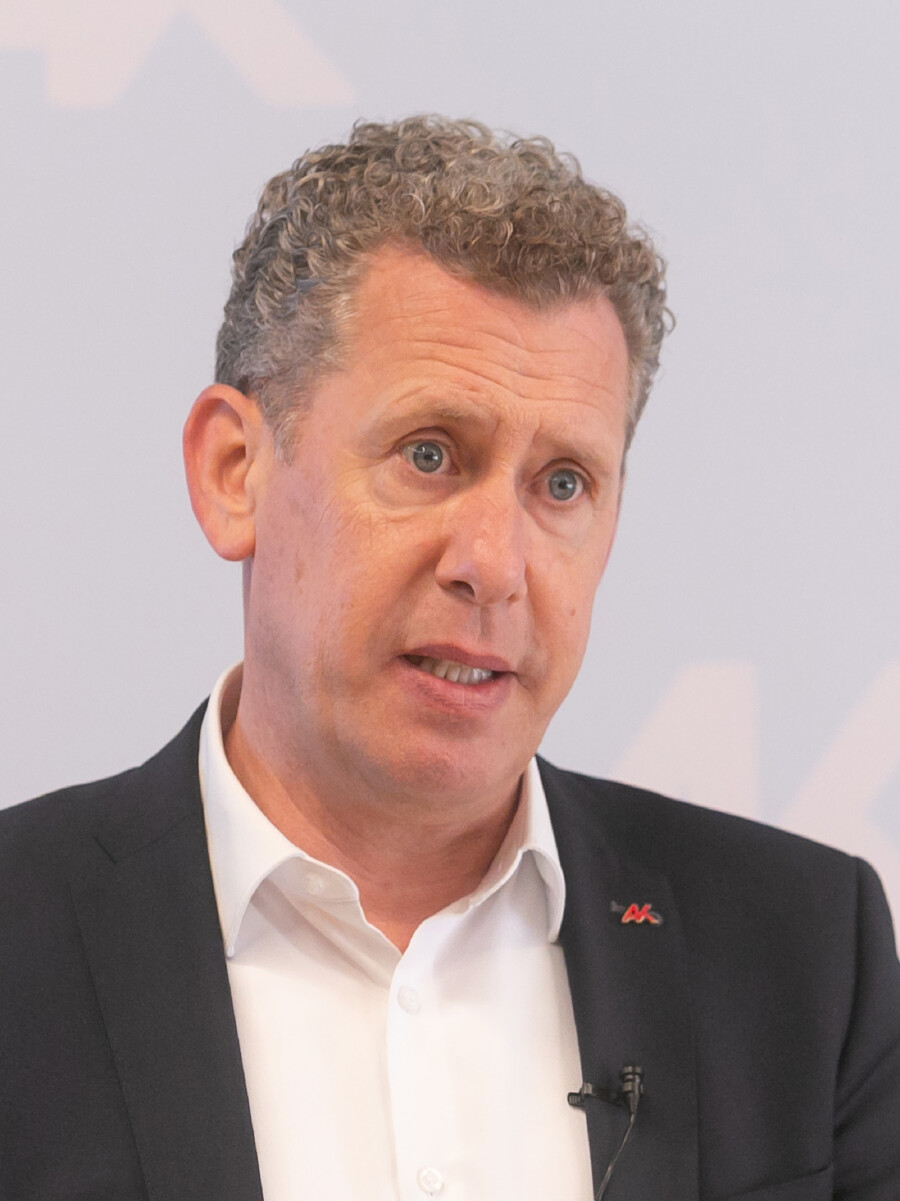 Portr&auml;tfoto von Bernhard Heinzle, Pr&auml;sident der Arbeiterkammer Vorarlberg. Er spricht, tr&auml;gt ein wei&szlig;es Hemd unter einem dunklen Sakko mit einem AK-Pin am Revers sowie ein Ansteckmikrofon. Er hat graues, lockiges Haar. Der Hintergrund ist hell und schlicht. Foto: Dietmar Mathis.