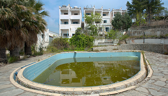 Ein verschmutzter Pool mit einem baufälligen Hotel im Hintergrund.
