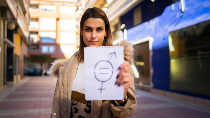 Eine Frau hält ein Zettel mit einem Symbol für Geschlechtergleichheit in die Höhe.