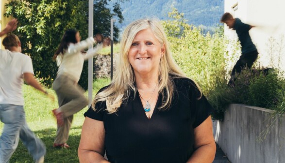Lächelnde Sozialbetreuerin mit türkisfarbener Halskette vor grüner Bergkulisse – engagiert im Beruf und ehrenamtlich als Gruppenleiterin bei den Pfadfindern aktiv, Symbol für soziale Verantwortung und Teamgeist.