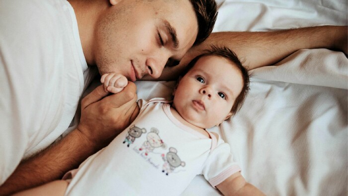 Ein Vater und sein Baby liegen entspannt auf einem Bett und genießen einen ruhigen Moment miteinander.