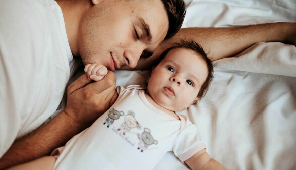 Ein Vater und sein Baby liegen entspannt auf einem Bett und genießen einen ruhigen Moment miteinander.