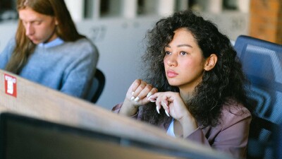 Junge Frau sitzt konzentriert an ihrem Arbeitsplatz im Büro und wirkt nachdenklich – Symbolbild dafür, Anzeichen von Gewalt oder Konflikten am Arbeitsplatz frühzeitig zu erkennen.