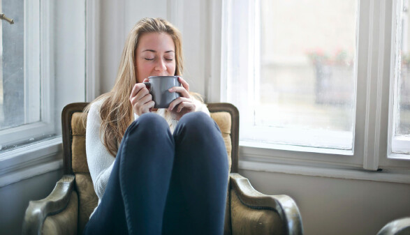 Eine blonde Frau sitzt mit einer Tasse Kaffee in einem Sessel.