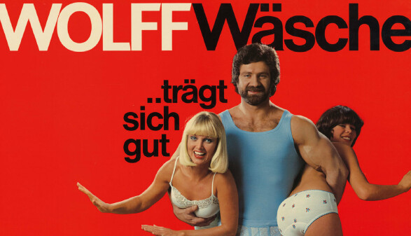 Das Bild zeigt ein altes Werbeplakat f&uuml;r Unterw&auml;sche, ein Mann tr&auml;gt darauf zwei Frauen in Unterw&auml;sche unter dem Arm.