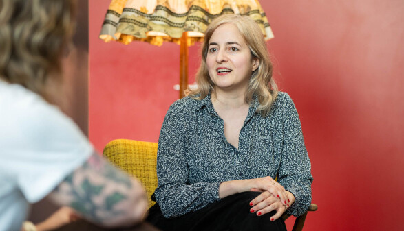 Eugenia Stamboliev sitzt im Gespr&auml;ch auf einem gelben Sessel vor einer roten Wand und spricht engagiert in Richtung ihres Gegen&uuml;bers.