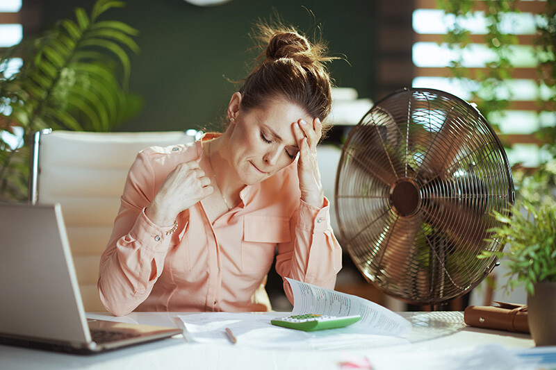 Eine Frau sitzt an einem Schreibtisch vor einem Ventilator.