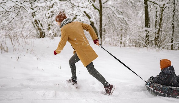 Ein Mann zieht ein Kind auf einem Reifen durch den Schnee.