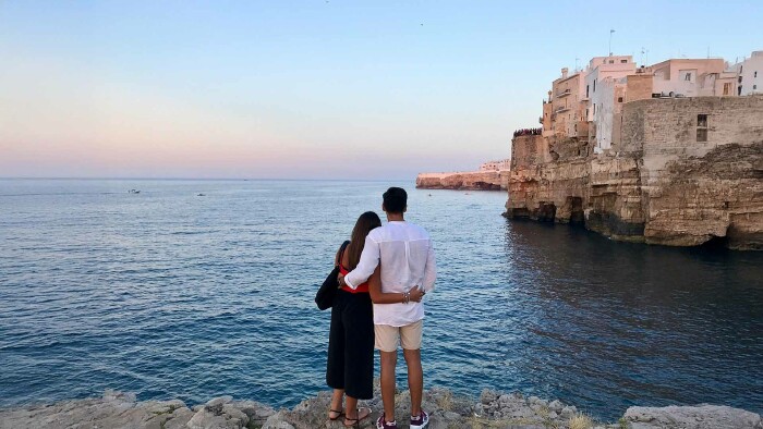 Paar blickt auf das Meer vor malerischen Felsklippen in Italien – Tipps zur sicheren Urlaubsbuchung für unbeschwerte Reisen.