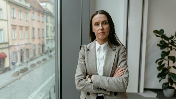 Businessfrau mit verschränkten Armen vor Fenster mit Stadtblick – Symbolbild für Equal Pay Day, Gehaltsunterschiede zwischen Männern und Frauen, und berufliche Gleichstellung im modernen Arbeitsumfeld