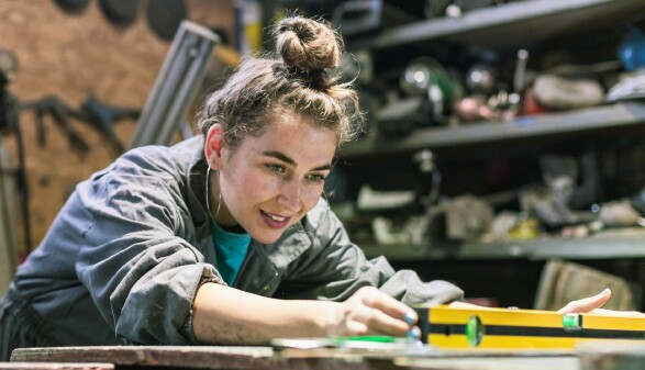  Eine Frau arbeitet konzentriert an einem Projekt in einer Werkstatt, umgeben von Werkzeugen und Materialien.