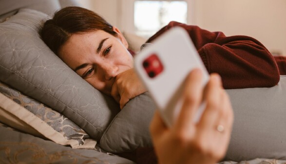Eine junge Frau liebt im Bett und schaut auf ihr Handy