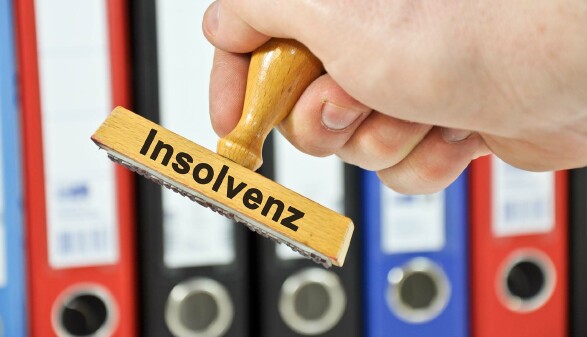 Das Bild zeigt eine Hand, die einen Holzstempel mit der Aufschrift „Insolvenz“ hält.