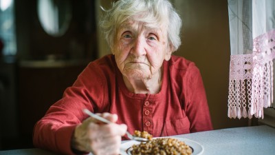 Eine ältere, von Armut betroffene Frau sitzt am Tisch und ist aus einem Teller © De Visu, Adobe Stock
