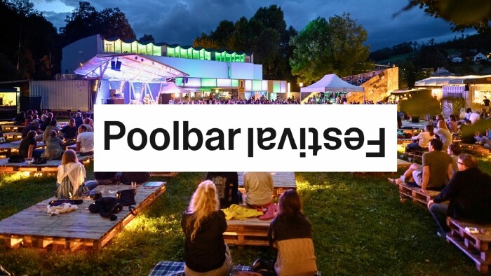 Au&szlig;enaufnahme des poolbar Festivals im Reichenfeld. Menschen sitzen gem&uuml;tlich auf B&auml;nken und Liegen. In der Mitte der Schriftzug: Poolbar Festival