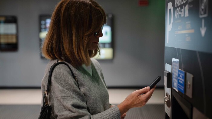 Eine Frau scannt einen QR-Code an einem Parkautomaten in einem Parkhaus.