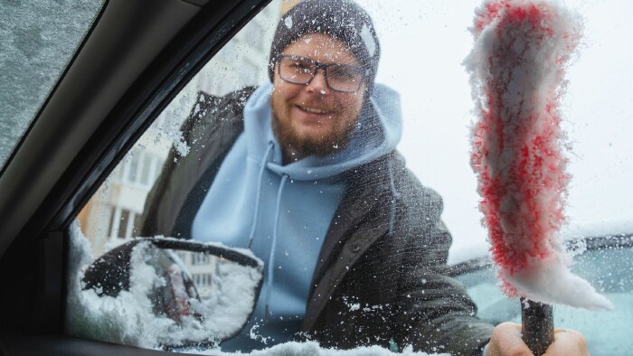 Ein Mann reinigt sein Auto mit einer Schneebürste, um Schnee und Eis zu entfernen.