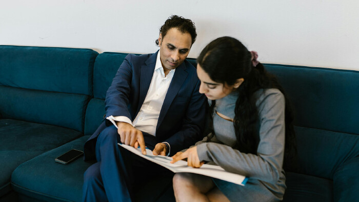 Sexuelle Belästigung beginnt nicht erst bei körperlichen Übergriffen. Bereits jedes unerwünschte, sexuell bestimmte Verhalten fällt darunter. © RDNE stock project, Pexels Ein Mann im Anzug und eine jüngere Frau im Kleid sitzen auf einem Sofa. Der Mann beugt sich zur Frau hinüber und deutet auf den Ordner auf dem Schoß der Frau.