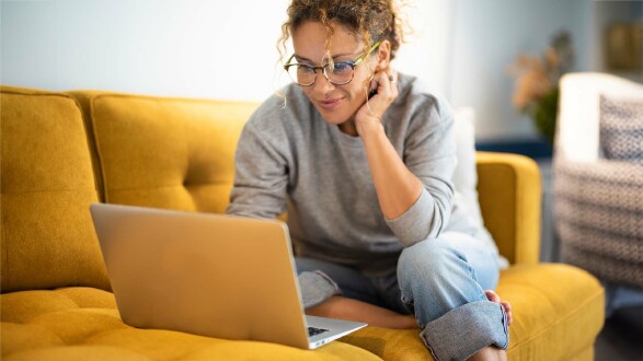 Eine Frau sitzt auf einer Couch am Laptop.