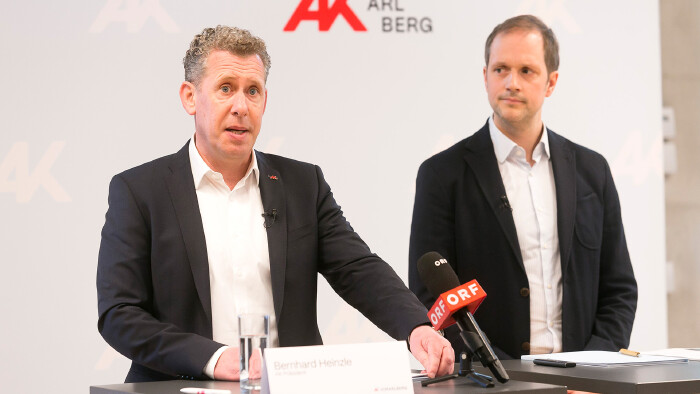 Pressekonferenz der Arbeiterkammer Vorarlberg: AK-Pr&auml;sident Bernhard Heinzle (links) spricht an einem Tisch mit einem ORF-Mikrofon, neben ihm steht Michael Klien vom WIFO (rechts). Im Hintergrund ist das Logo der AK Vorarlberg zu sehen.