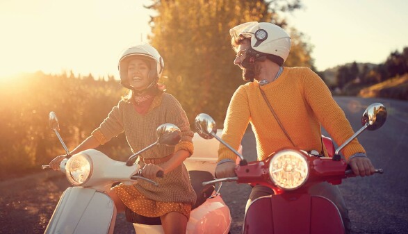 Junges Paar auf Motorrollern bei Sonnenuntergang – Italienurlaub 2025 mit neuen Verkehrsregeln für Roller, Auto und Fahrrad