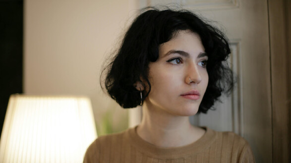 Portr&auml;t einer jungen Person mit kurzem dunklem Haar, die nachdenklich zur Seite blickt; ruhige Innenraumszene ohne sichtbare Gefahren &ndash; kann symbolisch f&uuml;r Unsicherheit oder Sorgen etwa vor Krieg und Unruhen am Urlaubsort stehen.