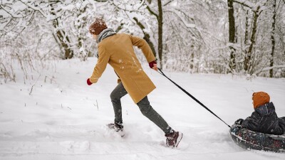 Ein Mann zieht ein Kind auf einem Reifen durch den Schnee.