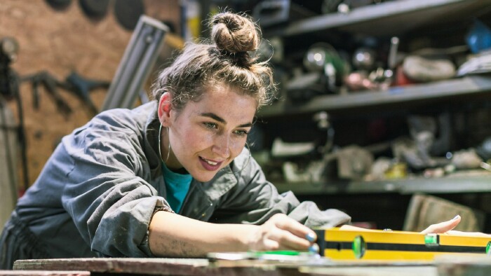  Eine Frau arbeitet konzentriert an einem Projekt in einer Werkstatt, umgeben von Werkzeugen und Materialien.