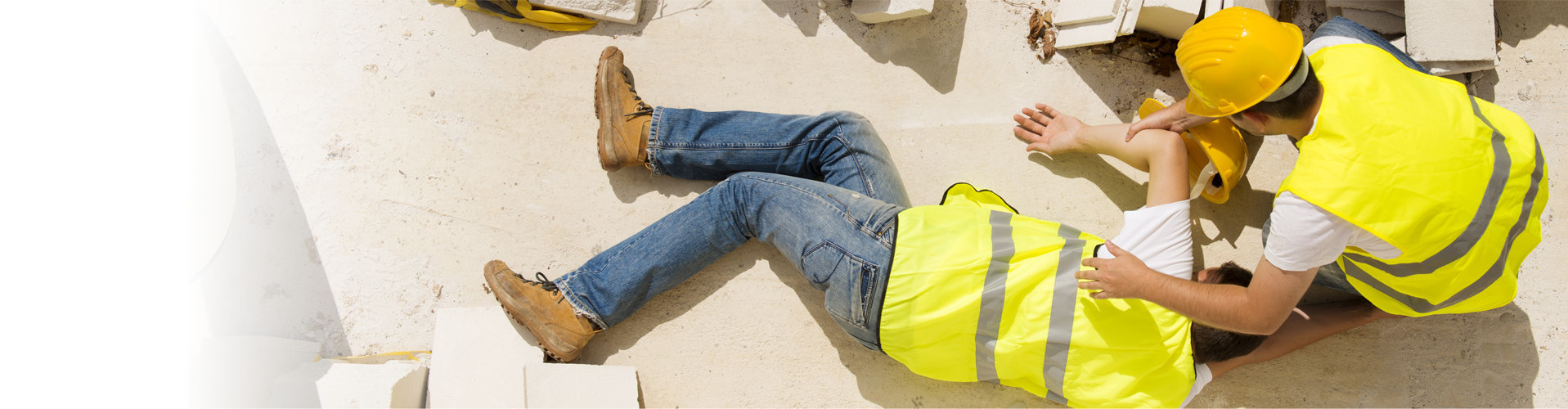 Ein Arbeiter auf der Baustelle beugt sich über einen zweiten Arbeiter, der am Boden liegt