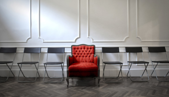 Ein roter, üppiger Sessel inmitten einer Reihe karger Stühle © ﻿﻿olly, Adobe Stock