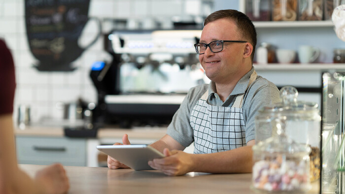 Junger Mann mit Down Syndrom bei der Arbeit in einem Kaffeehaus.