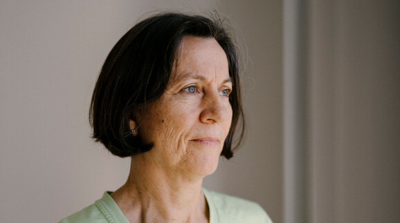Portr&auml;tfoto von Maria Lackner, Krankenschwester. Eine Frau mittleren Alters mit kurzem, dunklem Haar und blauen Augen blickt nachdenklich zur Seite. Sie tr&auml;gt ein hellgr&uuml;nes T-Shirt. Der Hintergrund ist schlicht und hell gehalten.