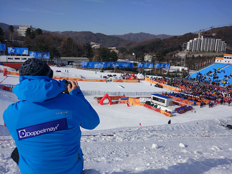 Bei den Olympischen Winterspielen 2018 war Elmar Röck als Seilbahntechniker ganz nah an den Wettkämpfen und Top-Athlet:innen. © Elmar Röck Elmar Röck sitzt im Schnee und blickt auf einen Wettkampf bei den Olympischen Winterspielen 2018.