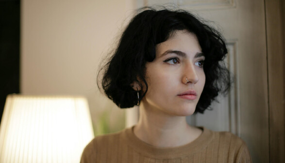 Portr&auml;t einer jungen Person mit kurzem dunklem Haar, die nachdenklich zur Seite blickt; ruhige Innenraumszene ohne sichtbare Gefahren &ndash; kann symbolisch f&uuml;r Unsicherheit oder Sorgen etwa vor Krieg und Unruhen am Urlaubsort stehen.