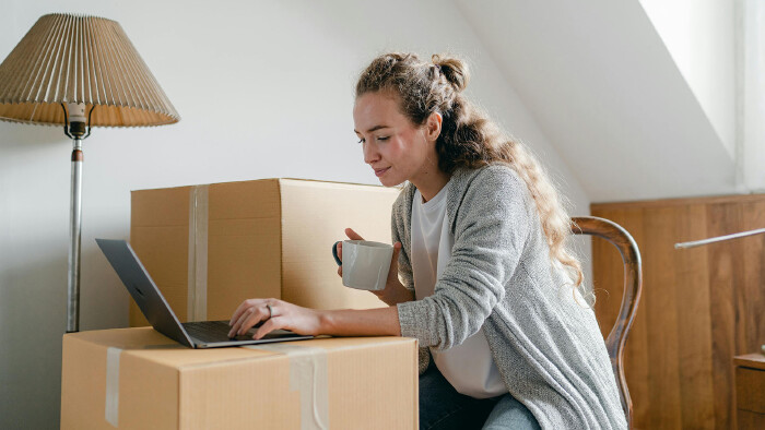 Eine Frau sitzt mit einem Laptop neben Umzugskartons.