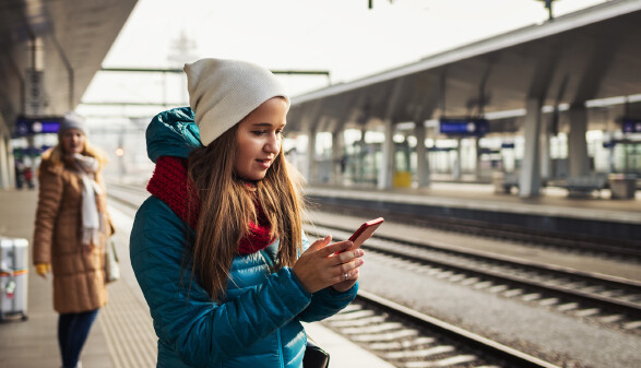 Frau wartet am Bahnsteig auf einen Zug und tippt etwas in ihr Handy