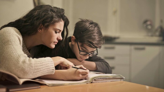 Immer mehr Kinder in Vorarlberg nehmen bezahlte Nachhilfe in Anspruch. Für viele Eltern bedeutet das eine große finanzielle Belastung. © Andrea Piacquadio, Pexels Ein Frau hilft einem Jungen beim Lernen und zeigt auf etwas in einem Lehrbuch, über das der Junge sich beugt.