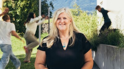 Lächelnde Sozialbetreuerin mit türkisfarbener Halskette vor grüner Bergkulisse – engagiert im Beruf und ehrenamtlich als Gruppenleiterin bei den Pfadfindern aktiv, Symbol für soziale Verantwortung und Teamgeist.