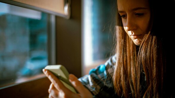 Person sitzt am Fenster und blickt gebannt auf Smartphone – symbolisiert die manipulative Wirkung von Dark Patterns in mobilen Apps, die Nutzer durch gezielte Designtricks an das Handy fesseln.