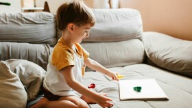 Ein kleiner Junge sitzt auf dem Sofa und beschäftigt sich mit einem Spielzeug.