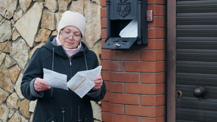 Eine ältere Frau steht vor dem Briefkasten und liest einen Brief.