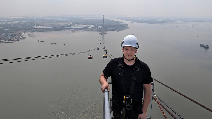 Elmar Röck arbeitet für Doppelmayr als Seilbahntechniker – zuletzt hier auf der mit 215 Metern höchsten Seilbahnstütze der Welt in Vietnam. © Elmar Röck Seilbahntechniker steht auf der Plattform an der Spitze einer Seilbahnstütze, unter ihm sieht man das Meer und im Hintergrund die Seilbahn, die bis zum Festland am Horizont reicht.
