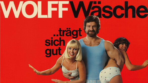 Das Bild zeigt ein altes Werbeplakat f&uuml;r Unterw&auml;sche, ein Mann tr&auml;gt darauf zwei Frauen in Unterw&auml;sche unter dem Arm.