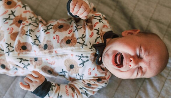 Ein weinendes Baby liegt auf einem Bett und zeigt seine Traurigkeit in einem emotionalen Moment.