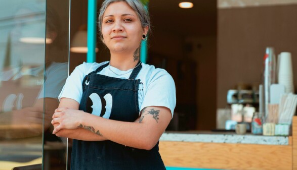 Eine Frau steht selbstbewusst vor einem Café und blickt in die Kamera