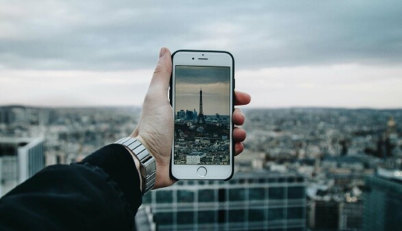 Eine Hand hält ein Smartphone, auf dem der Eiffelturm zu sehen ist.